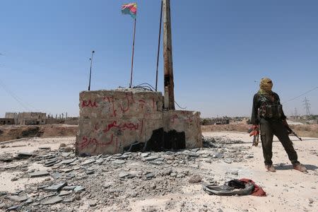 A Kurdish fighter stands with his weapons near a fluttering Kurdish flag in the Ghwairan neighborhood of Hasaka, Syria, August 23, 2016.REUTERS/Rodi Said