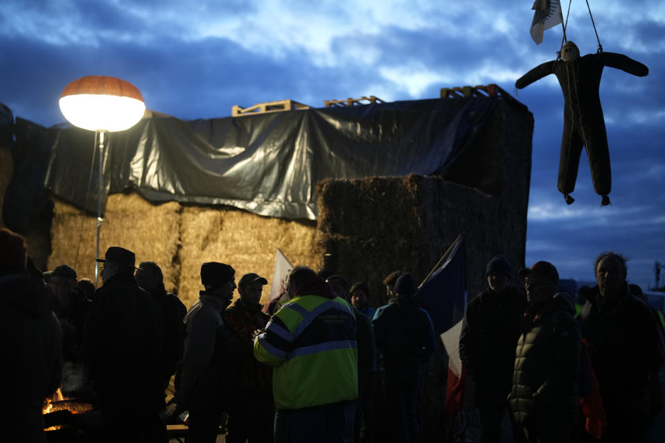 Farmers gather under a bridge where hangs a dummy farmer as they block a highway Tuesday, Jan. 30, 2024 in Jossigny, east of Paris. With protesting farmers camped out at barricades around Paris, France's government hoped to calm their anger with more concessions Tuesday to their complaints that growing and rearing food has become too difficult and not sufficiently lucrative. (AP Photo/Christophe Ena)