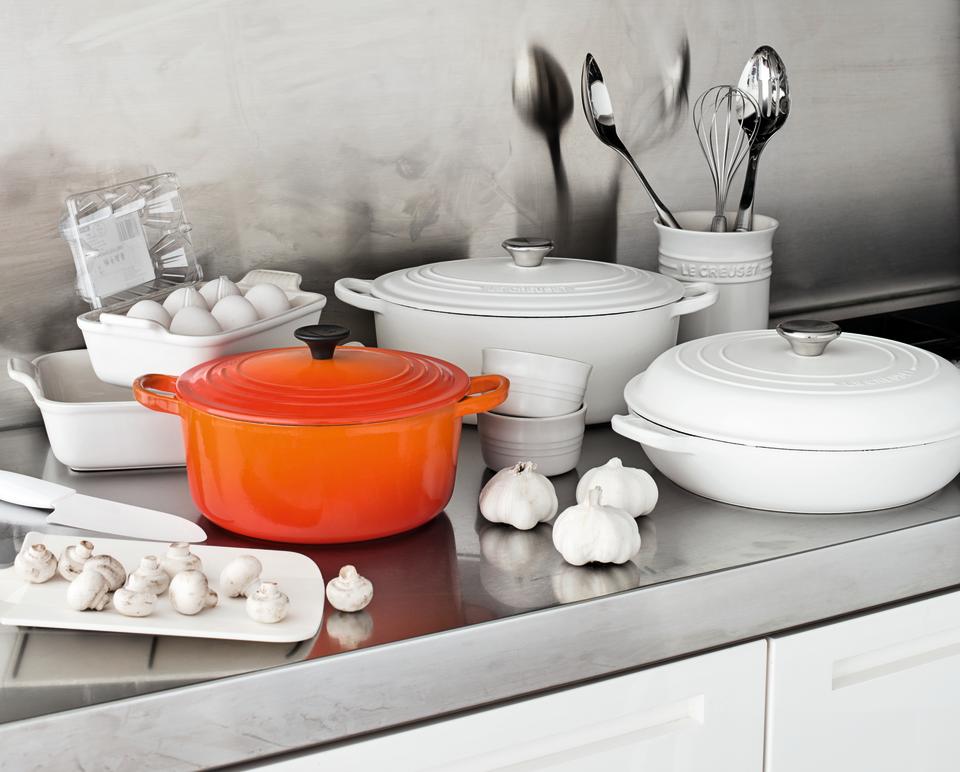 A kitchen countertop covered with cast iron cookware in white and orange