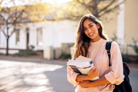 Smiling young female with backpack holding books