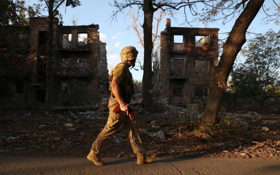 A solitary soldier walks past ruined buildings carrying an assault rifle