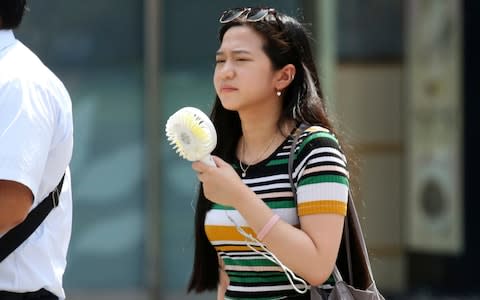 A woman holds a portable fan at a business district in Tokyo on Monday - Credit:  Koji Sasahara/AP