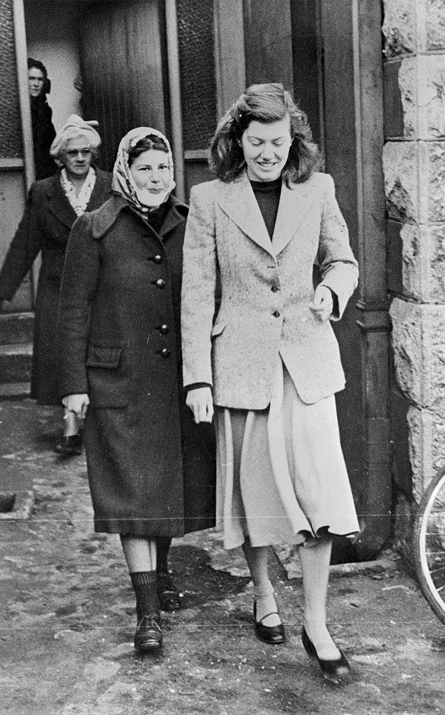 black and white photo of women walking out of a home