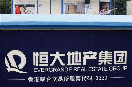 A labourer (R) gestures to his colleague outside their dormitory at a residential construction site of Evergrande, one of the biggest Chinese developers, near a wall painted with the company logo, in Guangzhou, Guangdong province in this June 22, 2012 file photo. REUTERS/Stringer/Files
