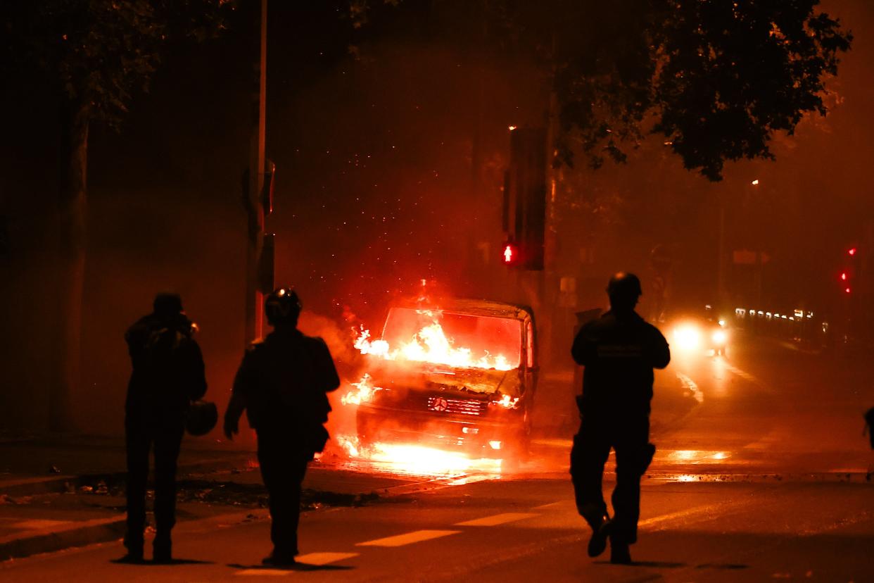 People walk next to a car burned during clashes between protesters and riot police in Nanterre, near Paris (EPA)