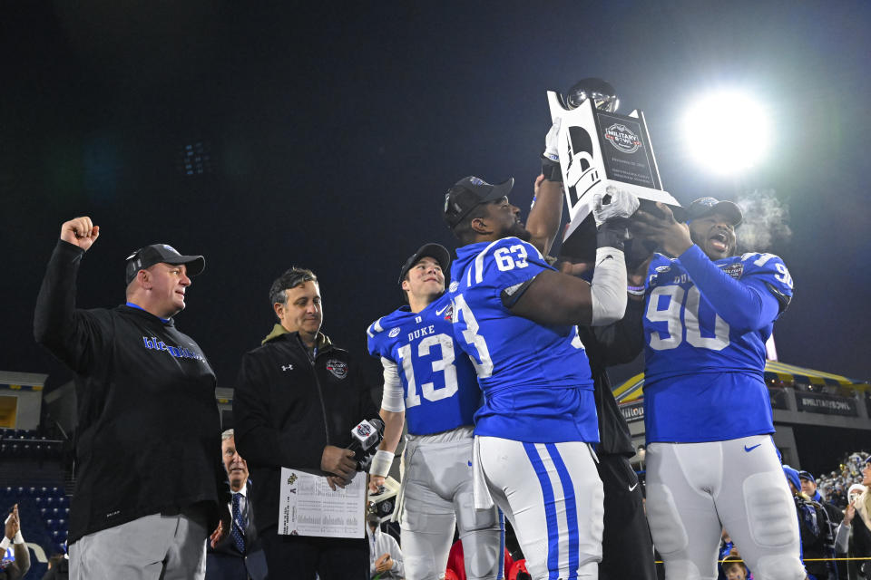 Duke offensive lineman Jacob Monk (63), defensive tackle DeWayne Carter (90) and quarterback Riley Leonard (13) hold the Military Bowl trophy as head coach Mike Elko, left, cheers after the Military Bowl NCAA college football game against UCF, Wednesday, Dec. 28, 2022, in Annapolis, Md. (AP Photo/Terrance Williams)