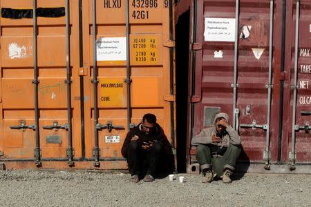 Two migrants rest next to containers at a makeshift camp for refugees and migrants at the Greek-Macedonian border near the village of Idomeni, Greece, April 28, 2016. REUTERS/Alexandros Avramidis