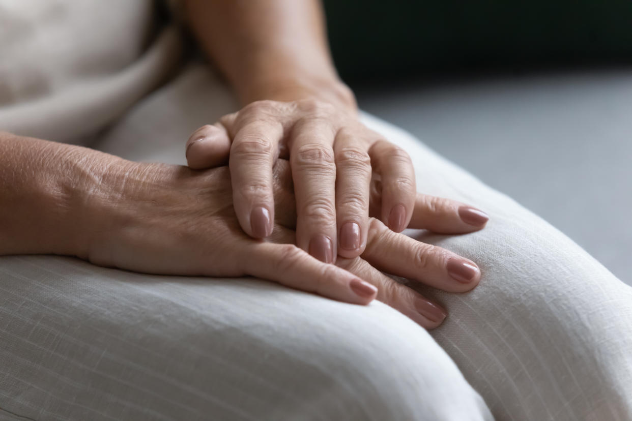 Lonely disabled elderly woman sit on sofa, close up view on hands folded palms on laps. Grandmother thinking about life feels abandoned, suffers from loneliness. Senile disease, health problem concept