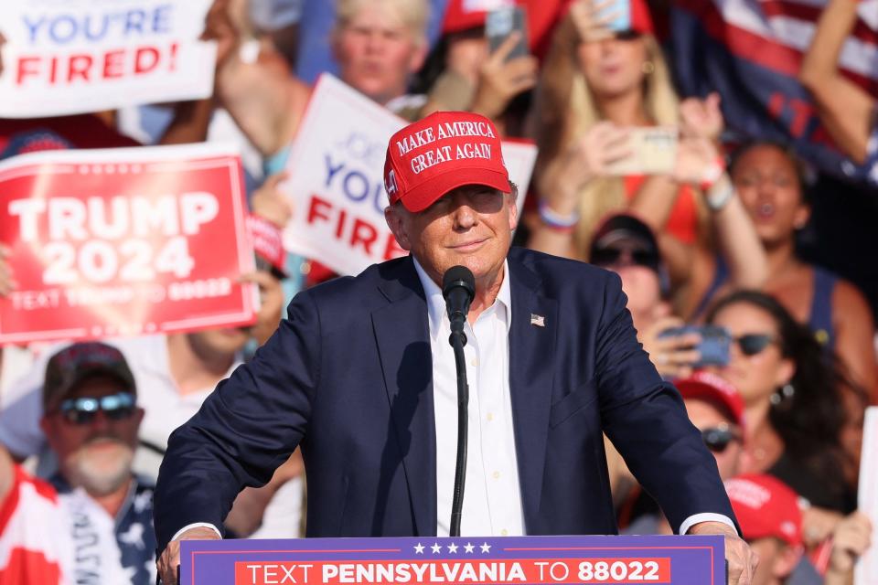 Trump stands on a stage at his rally, in a Make America Great Again hat, moments before pops rang out and Secret Service rushed the former president from the stage.