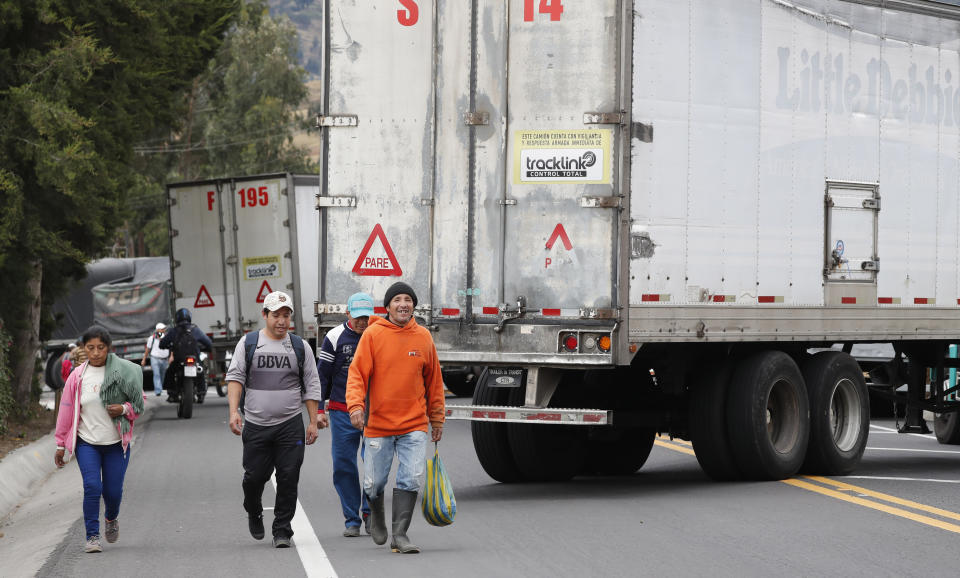 Residents walk along the Pan-American highway blocked by parked semi-trailer trucks during a nationwide transport strike that shut down taxi, bus and other services in response to a sudden rise in fuel prices, in Cangahua, Ecuador, Friday, Oct. 4, 2019. Ecuador's President Lenín Moreno, who earlier declared a state of emergency over the strike, vowed Friday that he wouldn't back down on the decision to end costly fuel subsidies, which doubled the price of diesel overnight and sharply raised gasoline prices. (AP Photo/Dolores Ochoa)