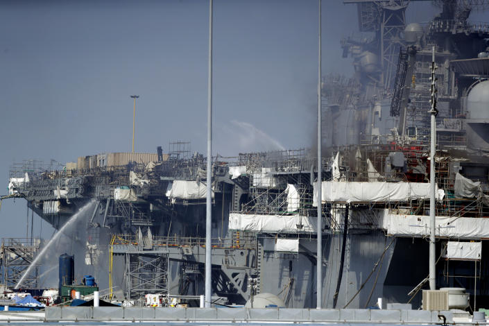FILE - Fire crews spray water from the dock onto the side of the USS Bonhomme Richard, in San Diego, July 12, 2020. No one disputes that the Navy shares blame for the loss of the USS Bonhomme Richard, the $1.2 billion amphibious assault ship that was consumed by flames in San Diego in July 2020 as officers failed to respond quickly and its crew struggled with broken equipment. But none of that would not have happened, according to prosecution closing arguments Thursday, Sept. 29, 2022, without Ryan Sawyer Mays. (AP Photo/Gregory Bull, File)
