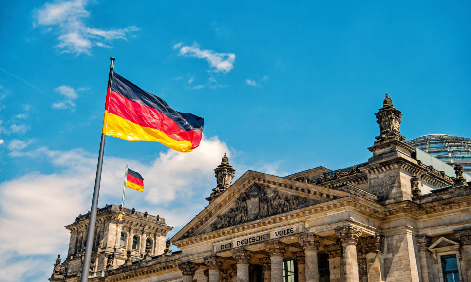 German flags waving in the wind at famous Reichstag building, seat of the German Parliament Deutscher Bundestag , on a sunny day with blue sky and clouds, central Berlin Mitte district, Germany