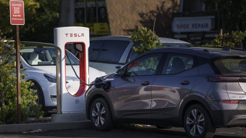 A white Tesla and gray Chevy Bolt charge at a Tesla supercharge