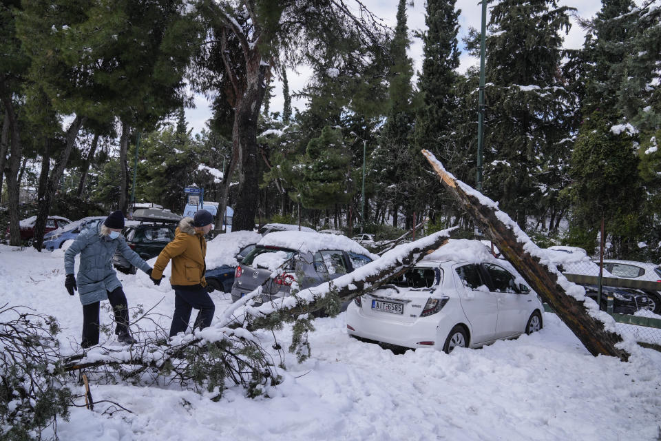 A couple walks past a fallen tree on a parked vehicle, in Athens, after a snowstorm on Tuesday, Jan. 25, 2022. A snowstorm of rare severity disrupted road and air traffic Monday in the Greek capital of Athens and neighboring Turkey's largest city of Istanbul, while most of Greece, including — unusually — several Aegean islands, and much of Turkey were blanketed by snow. (AP Photo/Thanassis Stavrakis)