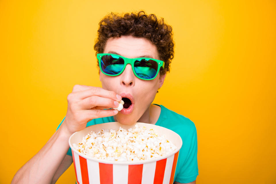 A male teenager in sunglasses wolfing down popcorn.