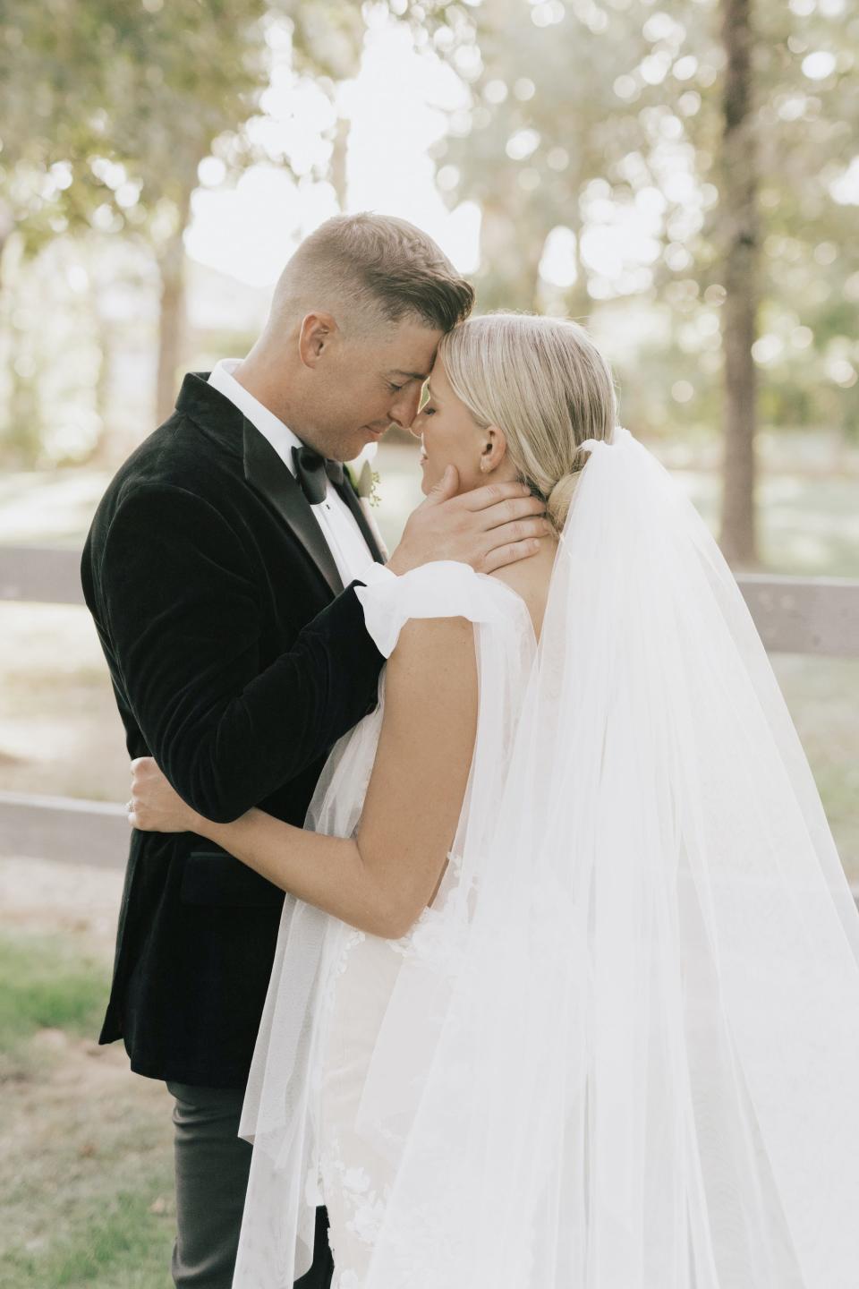 A bride and groom press their foreheads together and hug in a wooded area.