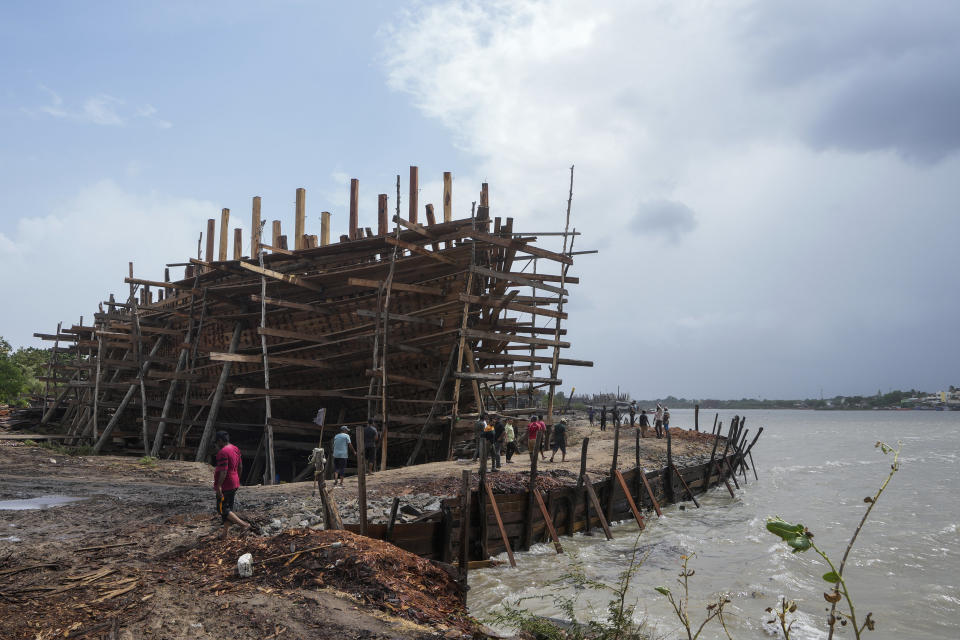 People walk past a vessel being made at Mandvi, a coastal town famous for boatmakers in Kutch district of Gujarat state, India, Wednesday, June 14, 2023. With Cyclone Biparjoy expected to make landfall Thursday evening, coastal regions of India and Pakistan are on high alert. (AP Photo/Ajit Solanki)