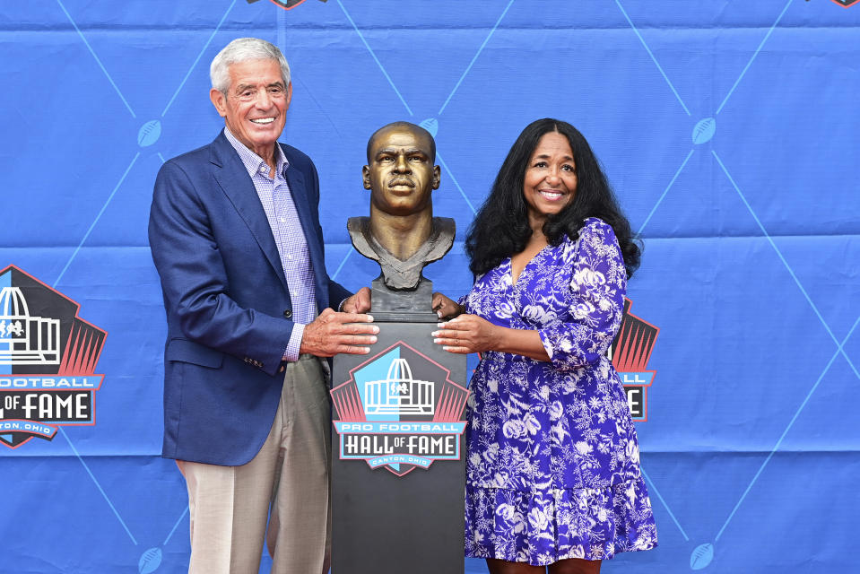 Melanie Mills, widow of former NFL player Sam Mills, right, and Jim Mora pose with his bust during an induction ceremony at the Pro Football Hall of Fame in Canton, Ohio, Saturday, Aug. 6, 2022. (AP Photo/David Dermer)