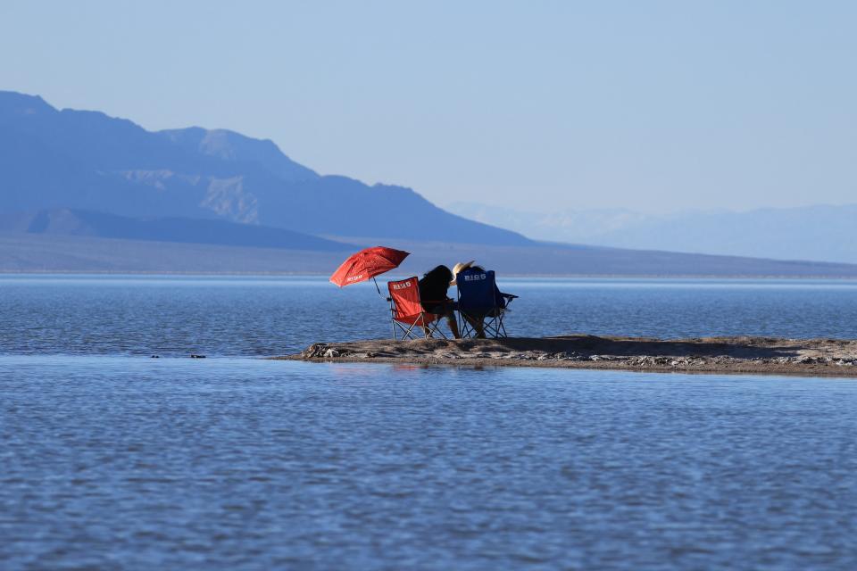 People relax by the water's edge as they enjoy the rare opportunity to see water during their visit to Badwater Basin, the normally driest place in the US, in Death Valley National Park on Sunday.