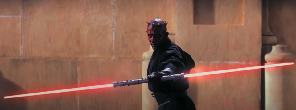 A man with a painted face wields a double-ended lightsaber