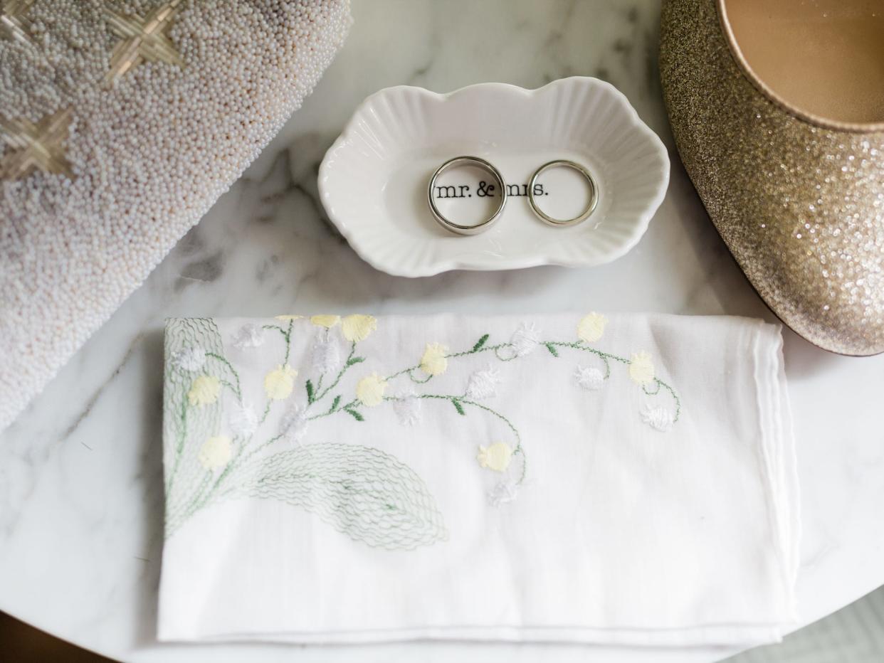 wedding rings. ina dish next to embroidered napkin and gold shoe for a wedding flatlay