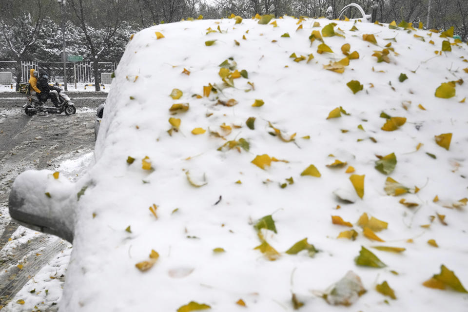 Residents past by a snow covered car in Beijing, China, Sunday, Nov. 7, 2021. An early-season snowstorm has blanketed much of northern China including the capital Beijing, prompting road closures and flight cancellations. (AP Photo/Ng Han Guan)