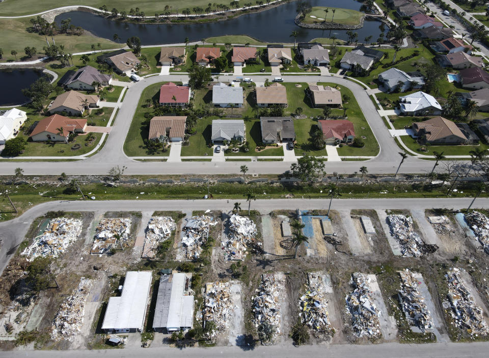 In this photo taken with a drone, the remains of homes demolished after sustaining heavy damage in Hurricane Ian are seen in Tropicana Sands mobile home park, bottom, in Fort Myers, Fla., Wednesday, May 10, 2023. More than seven months after the storm, crews continue removing debris after demolishing all but a handful of the hundreds of manufactured homes in the community marketed to active adults ages 55 and up. The state estimated the total insured loss from Ian in Florida was almost $14 billion, with more than 143,000 claims still open without payment or claims paid but not fully settled as of March 9. (AP Photo/Rebecca Blackwell)