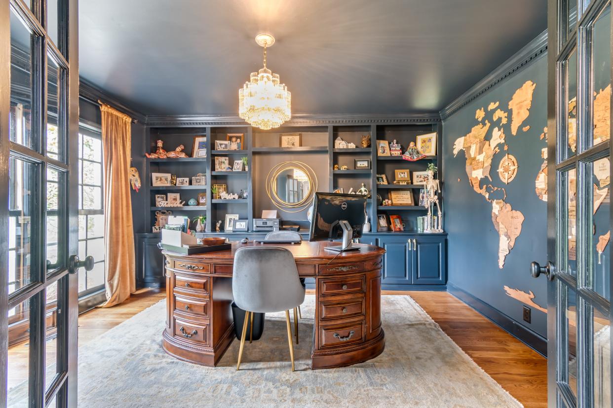 An adventurer’s home office at 8202 Foxview Court features French doors, built in bookshelves, dark blue walls, and a wood map of the world.