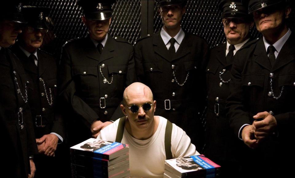 A bald man in sunglasses is surrounded by shadowed police officers