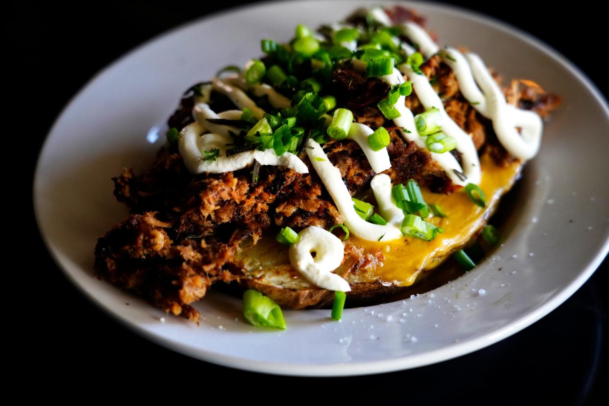 The loaded baked potato is served with smoked pork, queso/cheddar, butter, sour cream and green onion at Home Court Tavern.