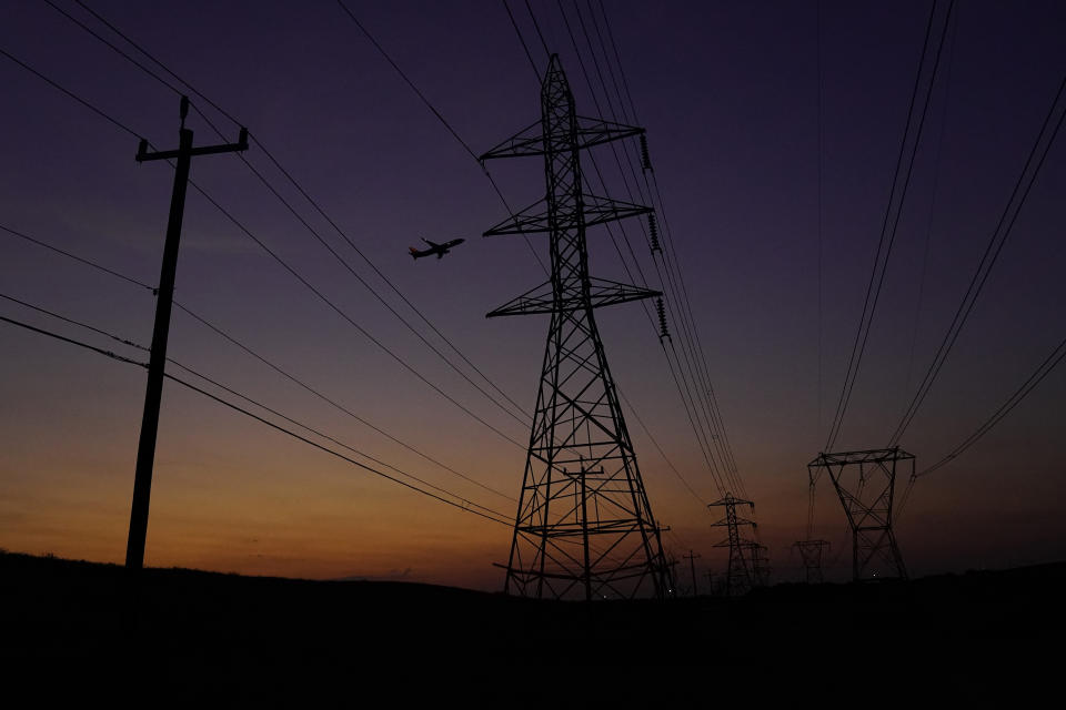An airplane passes power lines as the sun sets, Sunday, Aug. 20, 2023, in San Antonio. Triple digit temperatures continue to stress the power grid. (AP Photo/Eric Gay)