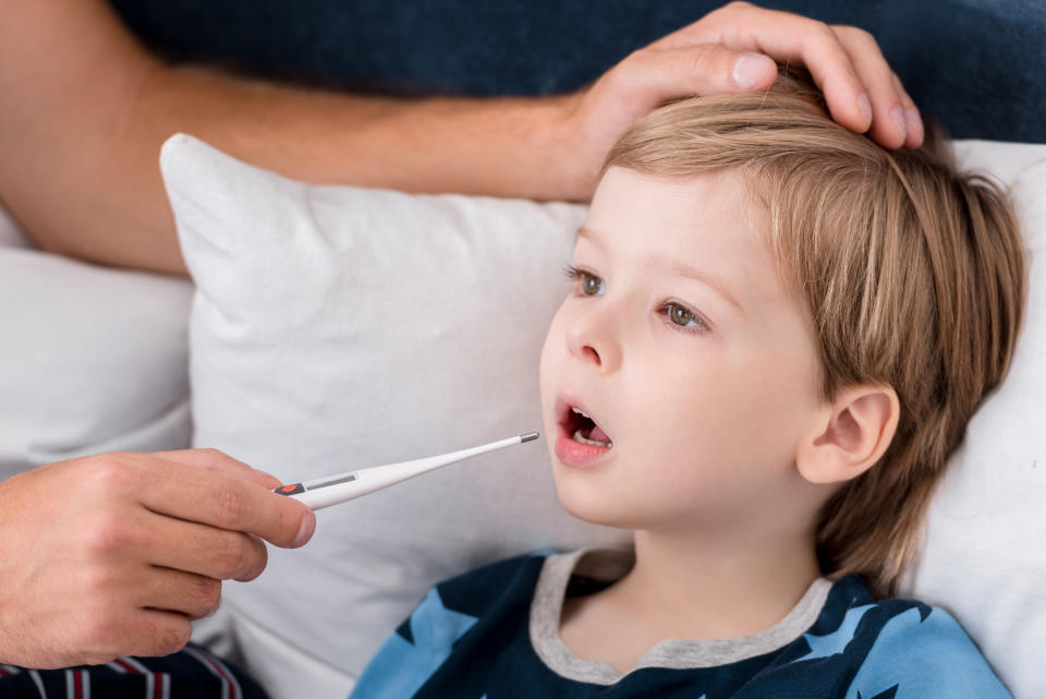 cropped shot of father checking oral temperature of son while he lying in bed