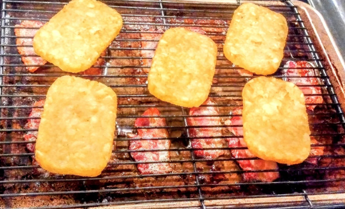 hashbrowns being grilled above bacon strips