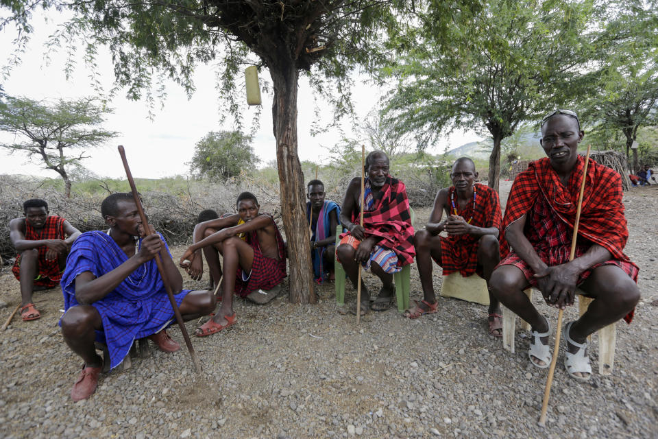 In this photo taken on Thursday, April 9, 2020, Maasai Village elder Letaari Salaash, center, sits under a tree with younger Maasai warriors at their village in Kajiado County in Kenya. The Maasai, a semi-nomadic indigenous group in Kenya and Tanzania, have been forced to halt important rituals that bring clans together due to the coronavirus, including the graduation of warriors into young men who can marry and own property. (AP Photo/Khalil Senosi)