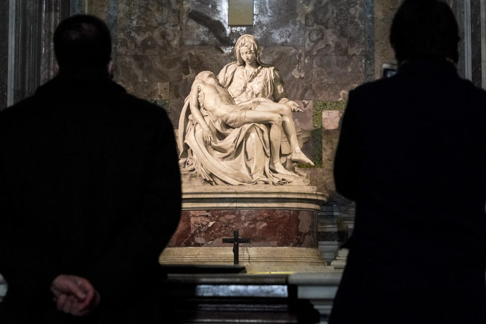 Visitors admire the marble sculpture "The Piety", made in 1499 by Italian sculptor Michelangelo Buonarroti, inside St. Peter's Basilica, at the Vatican, Monday, Dec. 14, 2020. Like elsewhere in Europe, museums and art galleries in Italy were closed this fall to contain the spread of COVID-19, meaning art lovers must rely on virtual tours to catch a glimpse of the treasures held by famous institutions such as the Uffizi in Florence and the Vatican Museums in Rome. However, some exquisite gems of Italy's cultural heritage remain on display in real life inside the country's churches, some of which have collections of renaissance art and iconography that would be the envy of any museum. (AP Photo/Andrew Medichini)