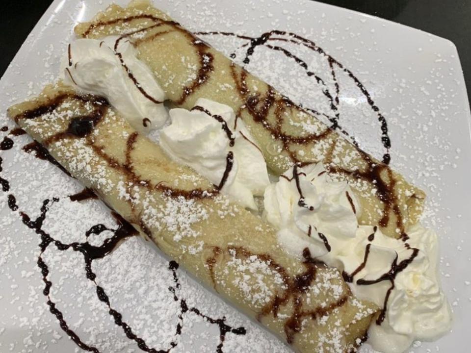 A crepe filled with cream with chocolate sauce drizzled over it.