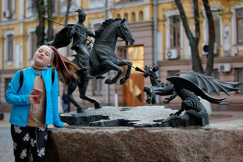 FILE - A child poses near a depiction of St. George slaying the dragon in Kyiv, Ukraine