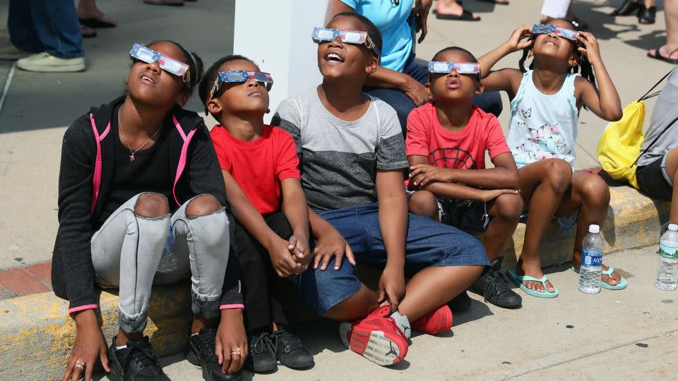 Spectators watch the partial solar eclipse while wearing protective glasses over Garden City, New York, on August 21, 2017. - Bruce Bennett/Getty Images