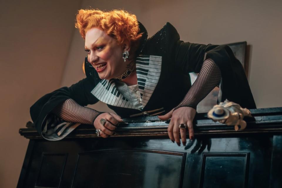 Jinkx Monsoon lays on top of a piano in a still from ‘Doctor Who’