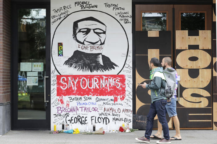 Pedestrians walk past a mural painted on plywood covering a window Monday, June 8, 2020, in Seattle, near the site of a demonstration the night before at a Seattle police precinct where protests continued over the death of George Floyd, a black man who was in police custody in Minneapolis. Just days after Seattle's mayor and police chief promised a month-long moratorium on using a type of tear gas to disperse protesters, the department used it again. (AP Photo/Elaine Thompson)