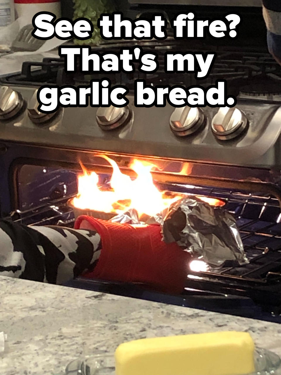 A kitchen oven with an open door, revealing flames engulfing garlic bread inside