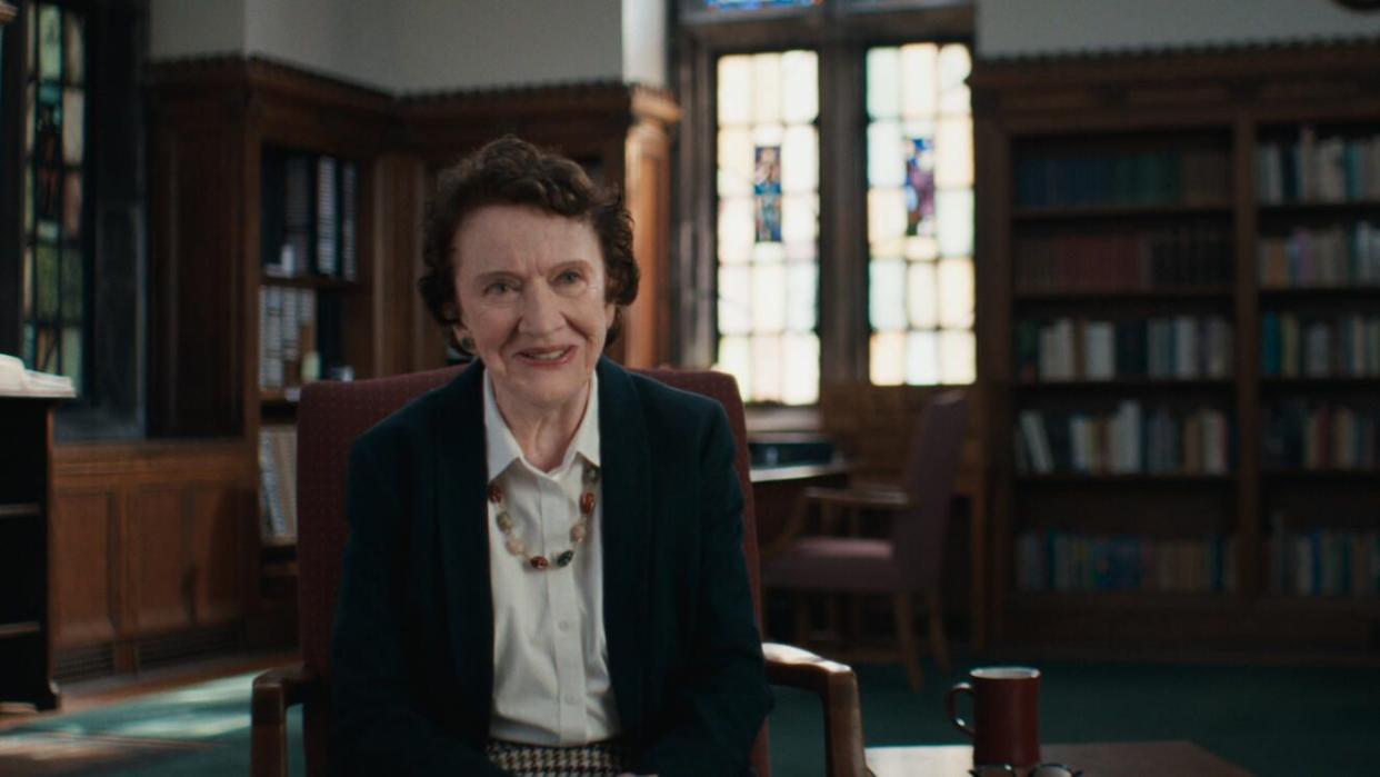 dr ann burgess sitting in a chair with book shelves and windows in the background of a study area