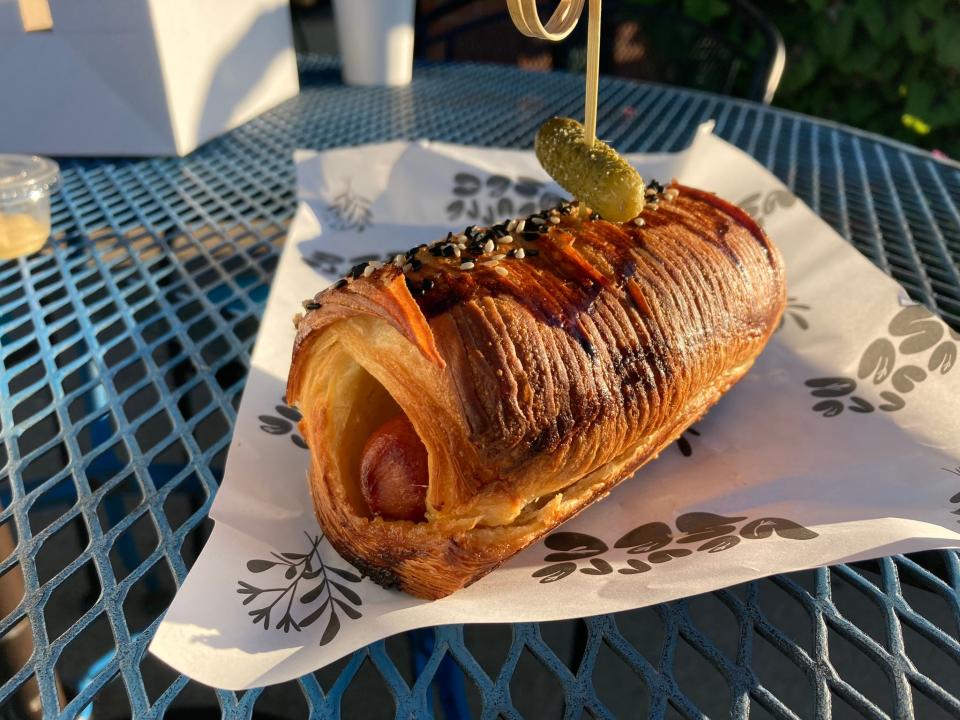 Croissant hot dog from Beurre Sec outside Lulu's Coffee and Bakehouse outside Lulu's Coffee and Bakehouse on Sept. 24, 2023. A cylindrical croissant houses an all-beef hot dog, caramelized onions and Dijon mustard with a gherkin on top.