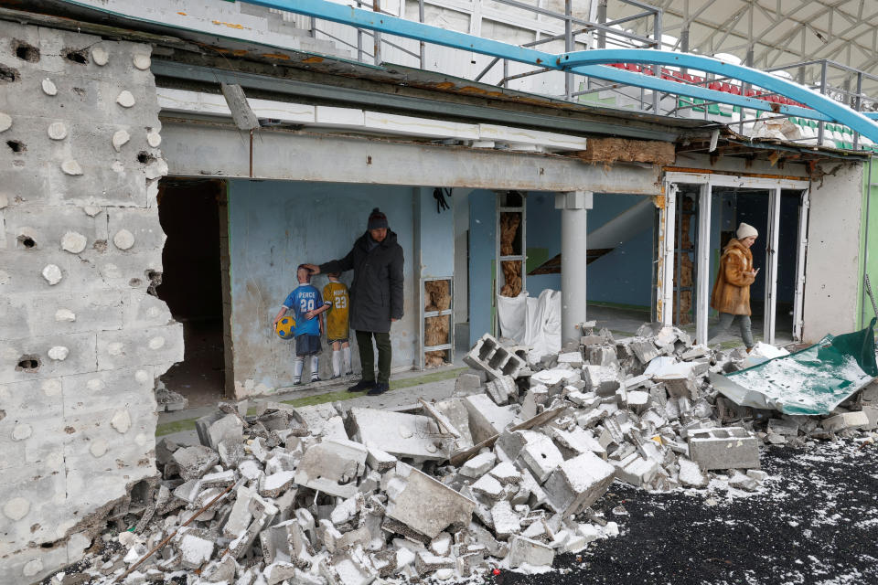 Kyiv resident Dmytro Melnyk stands next to an artwork of the famous street artist Tvboy, created on a wall of the town of Irpin's central stadium, which was damaged during Russia's attack on Ukraine, in the town of Irpin, outside Kyiv, Ukraine January 29, 2023. REUTERS/Valentyn Ogirenko