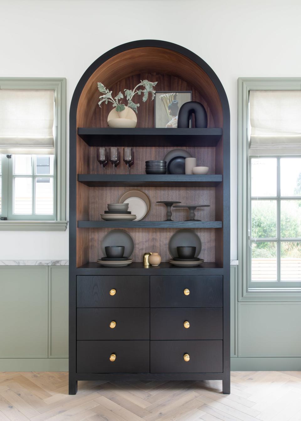 The walnut cabinet fits between two windows of varying heights. Not only does it trick the eye to make the area appear symmetrical, but because the kitchen has no upper cabinetry, it was important to have a functional piece.