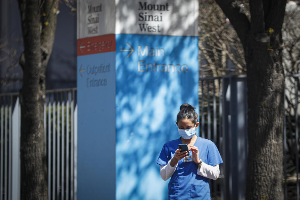 A medical worker uses her phone while wearing a surgical mask outside Mt. Sinai West, Thursday, March 26, 2020, in New York. The new coronavirus causes mild or moderate symptoms for most people, but for some, especially older adults and people with existing health problems, it can cause more severe illness or death. (AP Photo/John Minchillo)