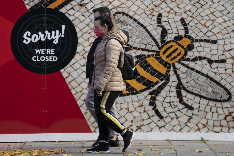 People walk by a sign in Manchester, England, Tuesday, Oct. 20, 2020. The British government appeared poised Tuesday to impose strict coronavirus restrictions on England's second-largest city after talks with officials in Greater Manchester failed to reach an agreement on financial support for people whose livelihoods will be hit by the new measures( AP Photo/Jon Super)