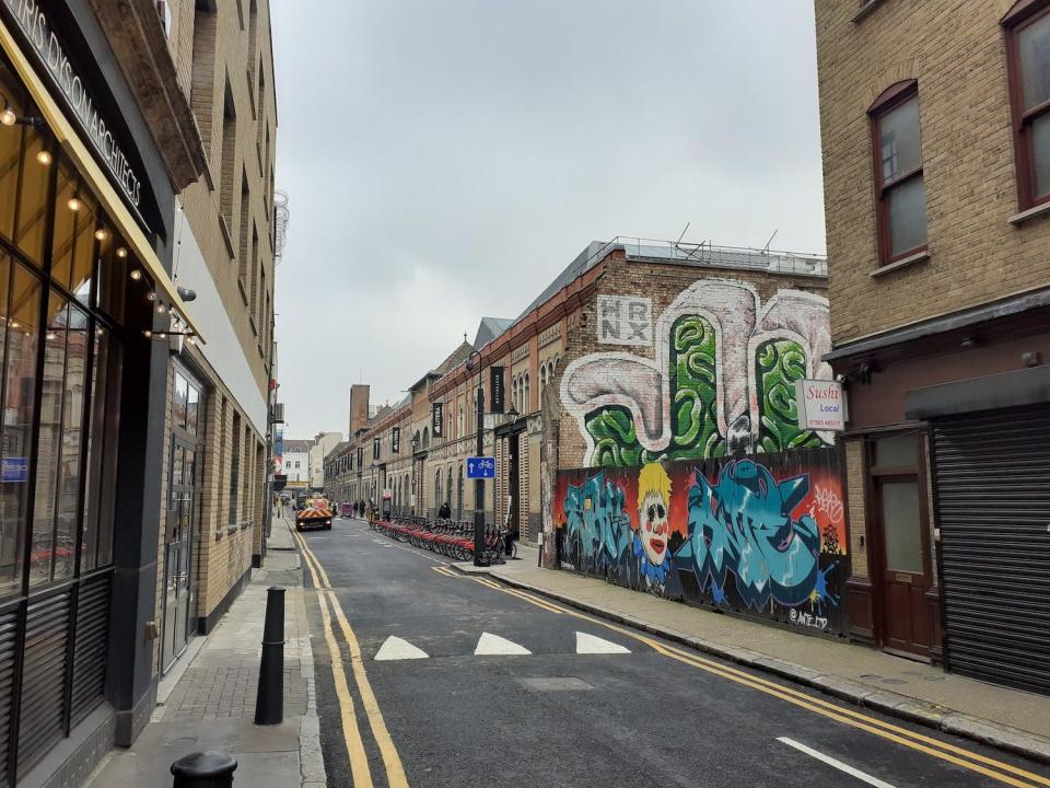 A shot of Fashion Street in London, it shows 'Boris bikes' and graffiti depicting Boris Johnson as a clown.