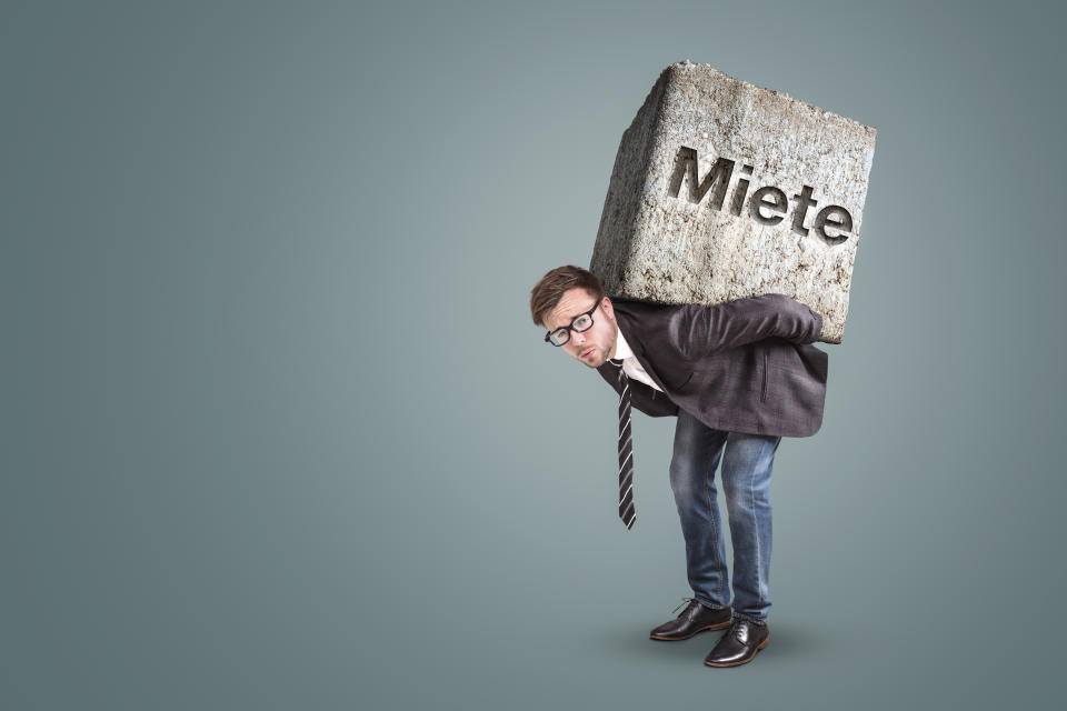 Concept of a man bending under the burden of a high rent. He is actually carrying a massive stone on his back with the German word "Miete" on it - meaning "rent".