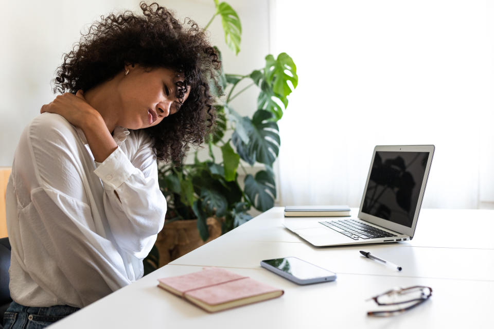 African American woman suffering from neck pain. Hispanic female working with laptop at home self massaging neck and shoulders. Body care